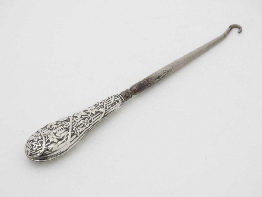 A silver handled button hook with embossed fruiting vine decoration